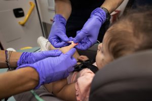 Gloved hands administering a bandage on a little girl's knee
