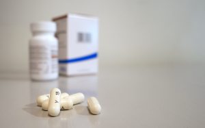 5 oblong cream-colored pills in the foreground, a pill bottle and box in the background